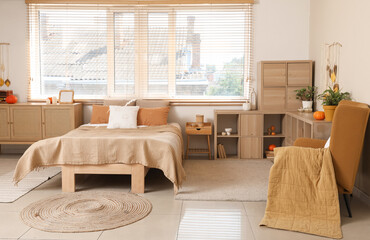 Interior of stylish bedroom with pumpkins and autumn decor on shelving unit near window