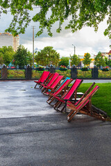 Wood-framed and fabric deck chairs on the asphalt path near the lawn in the park. Kharkiv city, no one after the rain