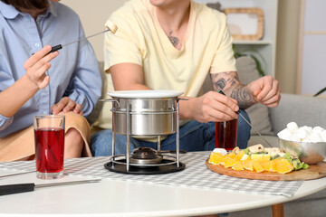 Young couple with glasses of wine dipping fresh bananas into chocolate fondue at home, closeup