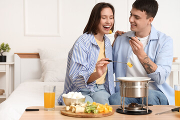Young happy couple with glasses of juice eating fresh oranges dipped in chocolate fondue at home