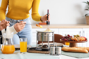 Young couple with glasses of juice dipping croutons into cheese fondue at home, closeup