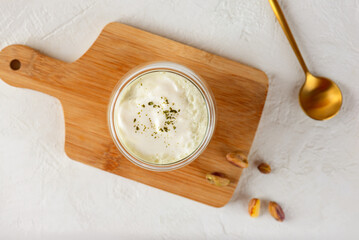 Pistachio matcha latte with whipped milk in a glass on a wooden board. Top view.