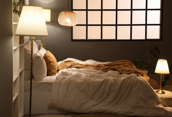 Interior of modern bedroom with cozy bed and glowing lamps at night
