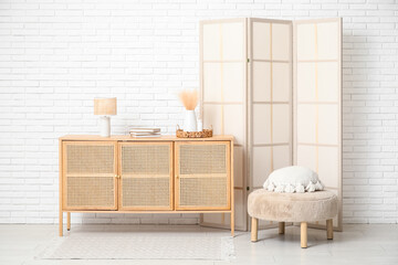 Interior of modern room with folding screen, pouf and chest of drawers
