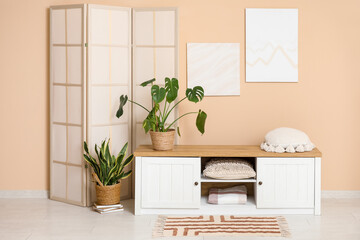 Interior of modern room with folding screen, houseplants and bench near beige wall