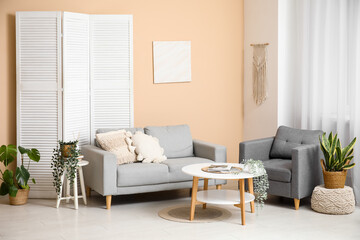 Table, sofa, armchair and folding screen near beige wall in interior of living room