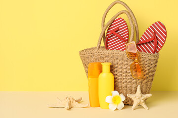 Wicker bag, bottles of sunscreen cream, starfishes and beach accessories on yellow background,...