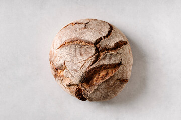  A single round sourdough loaf placed on a bright textured surface, highlighting natural cracks and rustic appearance