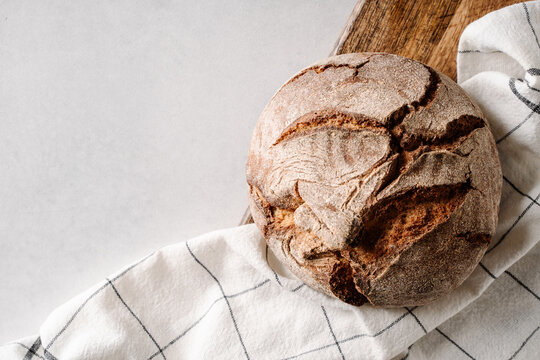 Crusty round sourdough bread resting on a wooden board with a white kitchen towel, showcasing rustic texture and artisan style