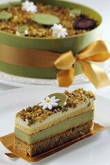 A delicate slice of layered green tea and pistachio cake, garnished with a white flower and...