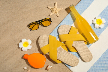 Bottle of sunscreen cream, flower and beach accessories on sand as background, closeup