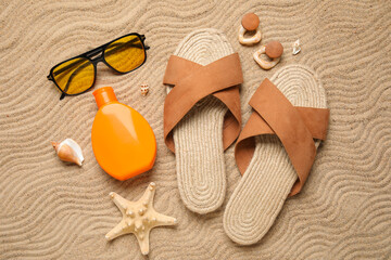Bottle of sunscreen cream, seashells and beach accessories on sand as background, closeup