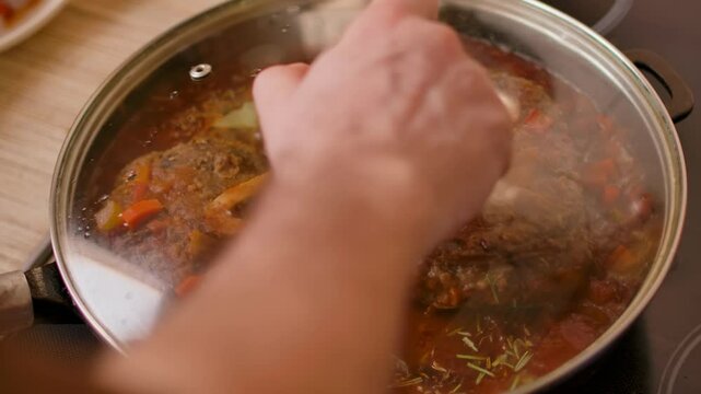 hand closes glass lid in which steak osso buco with vegetables is being fried. High quality 4k footage