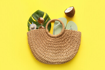 Summer composition with wicker bag, coconut and beach accessories on yellow background