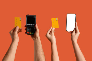 Hands with mobile phone, payment terminal and credit cards on orange background