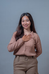 A young Indonesian woman smiling gently with a heartfelt expression, placing her hands on her chest...