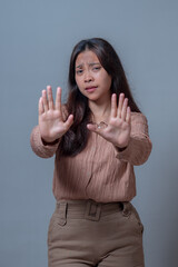 An Asian woman in a beige shirt and pants, holding both hands up with open palms, expressing a...