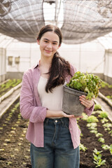 Teenage Asian female student wearing casual shirt holding potted lettuce plant while standing...
