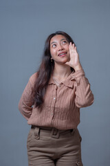 Young Indonesian woman posing with a cheerful expression while holding her hand to her mouth as if...