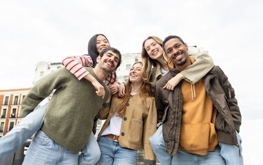 Multicultural group of young adults laughing and piggybacking in the city