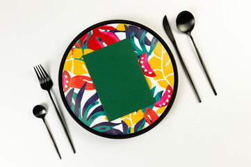 Top view of black tray, colorful plate, black cutlery on white background. Green card, exotic plant plate, summer picnic. Flat lay, copy space.