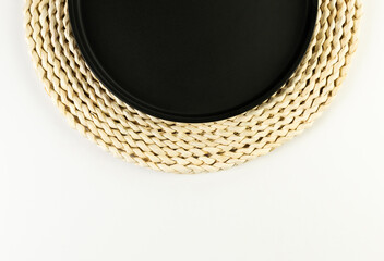 Top view of brown wicker table mat, black plate on white background. Straw round tray, flat lay, copy space. 