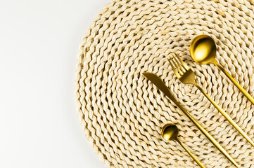 Top view of brown wicker table mat, gold cutlery on white background. Straw round tray, flat lay, copy space. 