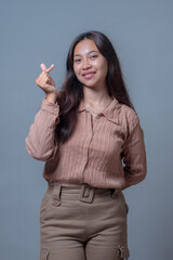 A young Indonesian woman smiles while making a heart gesture with her fingers. She is dressed in a...