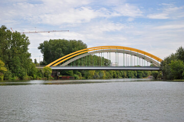 Modern Arched Steel Road Bridge Crossing Calm River with Tree Lined Riverbanks 