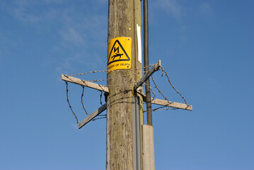 Timber Electricity Supply Pole with Danger Sign  and Anti Climb Barbed Wire seen against Blue Sky