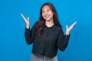 Happy young Asian woman with long hair wearing a black shirt poses against a blue background,...
