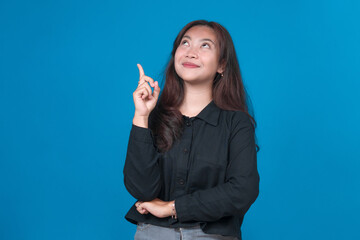 Young Asian woman in black shirt pointing upward with index finger while looking up, smiling with...