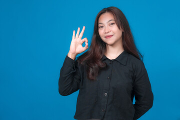 Young Asian woman in a black shirt showing an OK hand gesture with a confident smile, standing...