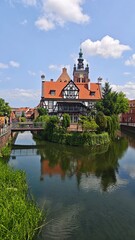 Fototapeta premium Historic half-timbered building with red tile roof and clock tower reflected in a calm river in Gdansk