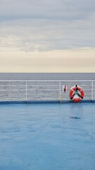 View of a calm sea from a ferry deck with a lifebuoy attached to the white railing. This image...