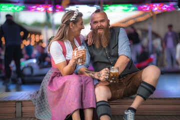 Bavarian couple in dirndl and lederhosen at the folk festival holding large mugs of German beer