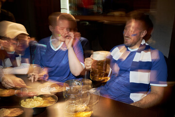 Group of young polyethnic male and female soccer fans celebrating together at table, smiling and...
