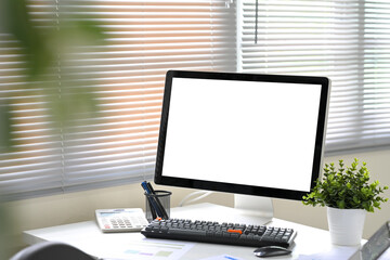Blank desktop computer screen on white office desk with calculator, and potted plant