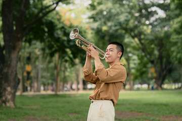 Young man playing trumpet outdoors in a peaceful green park © Prathankarnpap