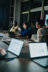 A diverse group of business people working late in a stylish office setting, focusing intently on...
