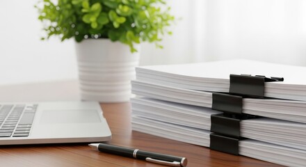 Organized stack of office documents secured with binder clips on a wooden desk surface next to
