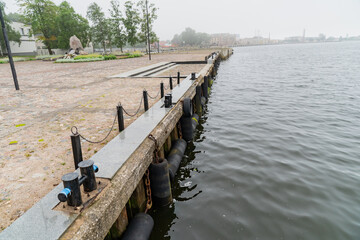 Harbor quay with metal bollards and chains along calm waterfront, industrial dockside...