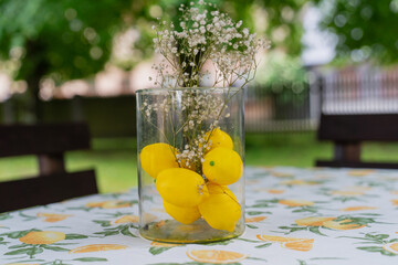 yellow lemons and delicate white flowers on lemon-patterned tablecloth, decorative centerpiece on...