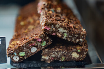 Chocolate dessert bars with colorful candy pieces and crunchy texture stacked on black tray, sweet snack or bakery treat