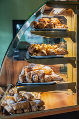 Bakery display case with trays of fresh croissants and assorted pastries, golden baked goods showcased in warm and inviting pastry shop interior