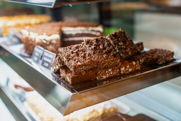 Bakery display case with stacked chocolate dessert bars and cakes, sweet baked goods on metal tray in pastry shop interior