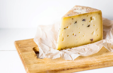 A piece of fresh, aged, natural farm cheese on parchment on a wooden board. Quality of farm-fresh agricultural products.