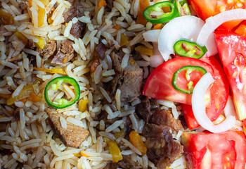 A rice dish with meat, garnished with a salad of chopped tomatoes, onions and hot green chili...
