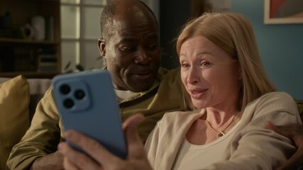 Rack focus shot of diverse senior couple speaking with relatives during video call using smartphone and waving goodbye with smile, Caucasian woman blowing kiss - Powered by Adobe