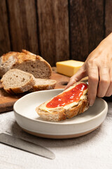 Hand holding a slice of bread with butter and strawberry jam